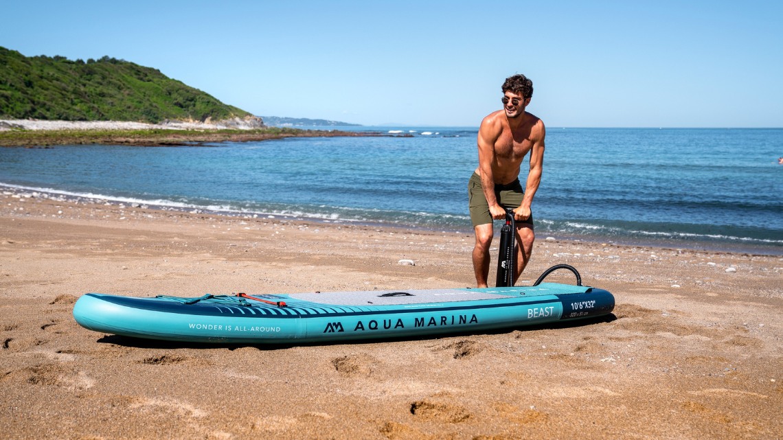 man pumping an inflatable sup board on the beach